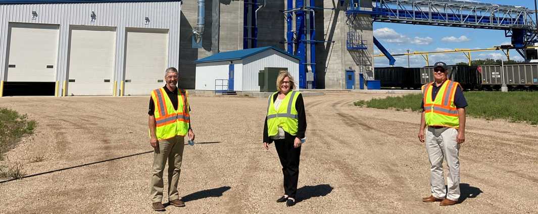 three people in reflective yellow vests standing in front of grain elevator